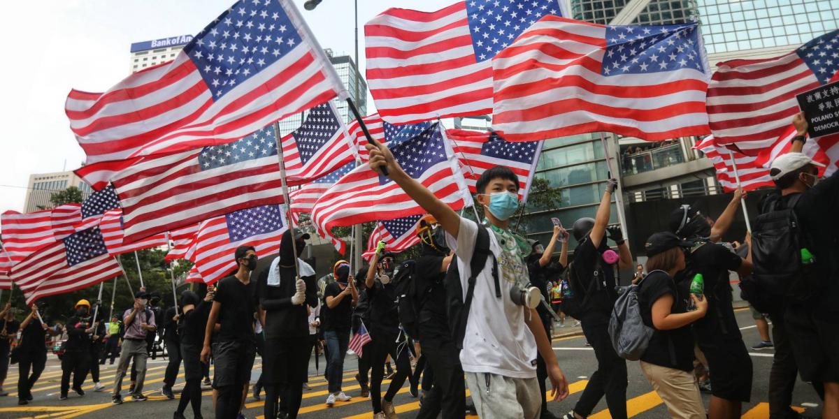 Hongkongi tüntetők vonulnak a város utcáin az amerikai konzulátus felé, kezükben amerikai zászlókkal 2019. szeptember 8-án