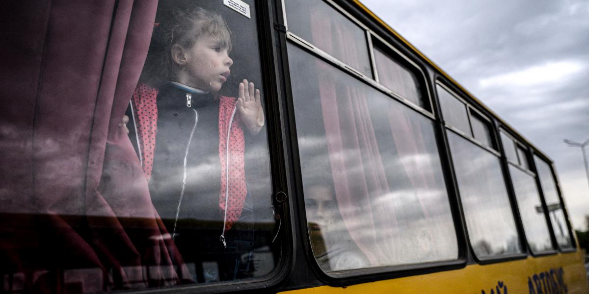 Egy lány néz ki egy buszból, miközben az orosz megszállás alatt álló zaporizzsjai területről származó családok érkeznek egy humanitárius konvojjal a belső menekültek regisztrációs és feldolgozó központjába Zaporizzsjában 2022. április 29-én, az Ukrajna el