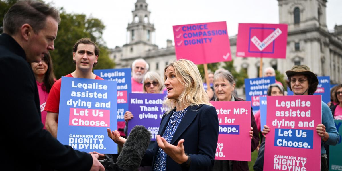 A törvényjavaslat szerdai benyújtásával egy időben a Méltósággal a Haldoklásban nevű szervezet demonstrációt tartott a Westminster-palota előtt az eutanázia legalizálása mellett (a képen Kim Leadbeater munkáspárti képviselő látható). A feliratokon ez áll: