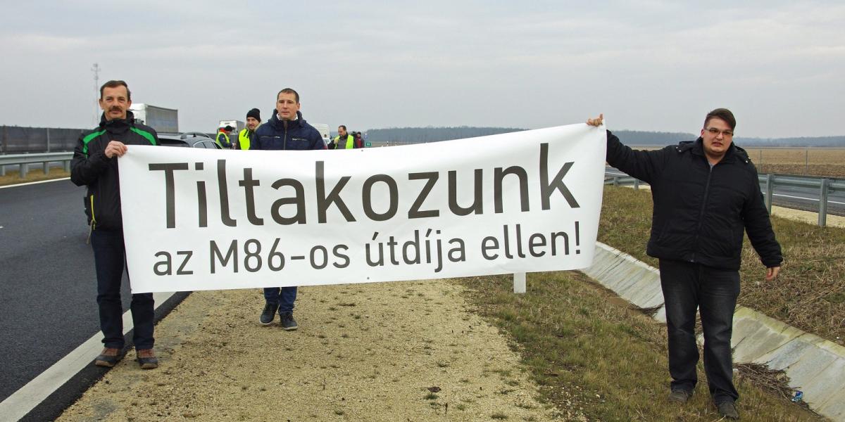 Résztvevők Tiltakozunk az M86-os útdíja ellen! feliratú transzparenst tartanak a kezükben Szombathely határában. MTI Fotó: Büki 