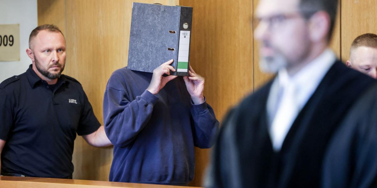 A vádlott ápoló egy irattartóval az arca előtt a tárgyalóteremben. 