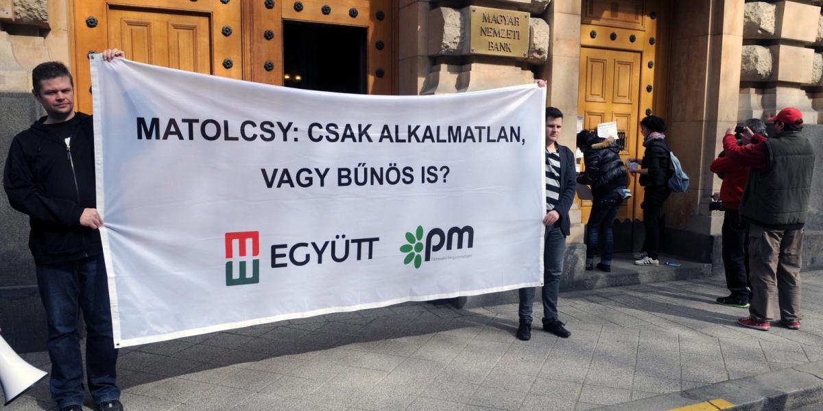 Az Együtt-PM szövetség aktivistái "Matolcsy: csak alkalmatlan vagy bűnös is?" feliratú molinót tartanak demonstrációjukon a Magy