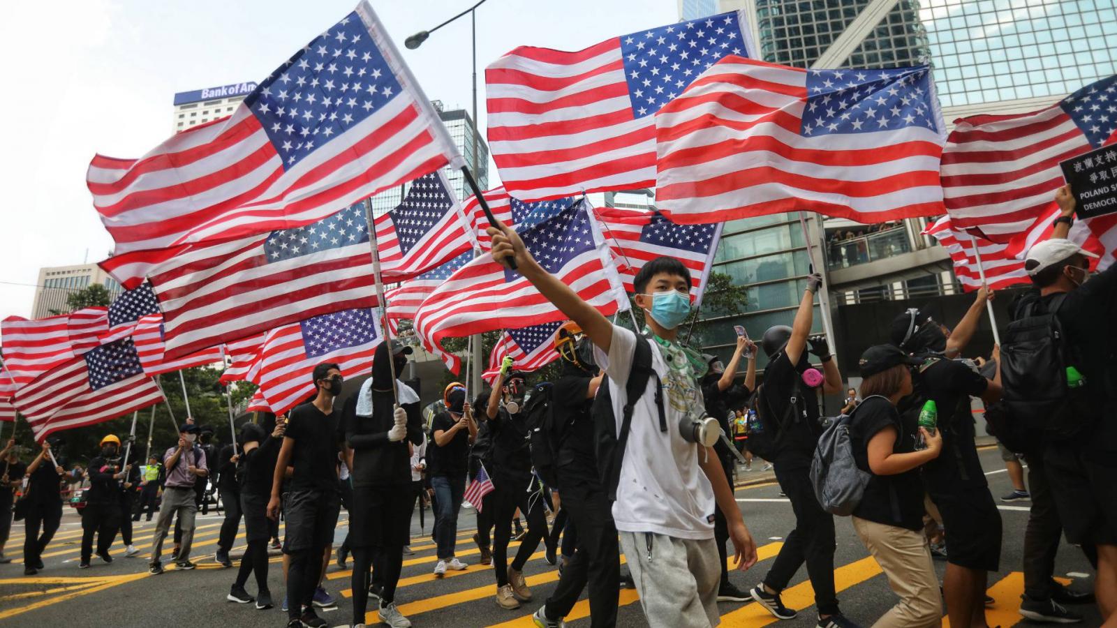 Hongkongi tüntetők vonulnak a város utcáin az amerikai konzulátus felé, kezükben amerikai zászlókkal 2019. szeptember 8-án