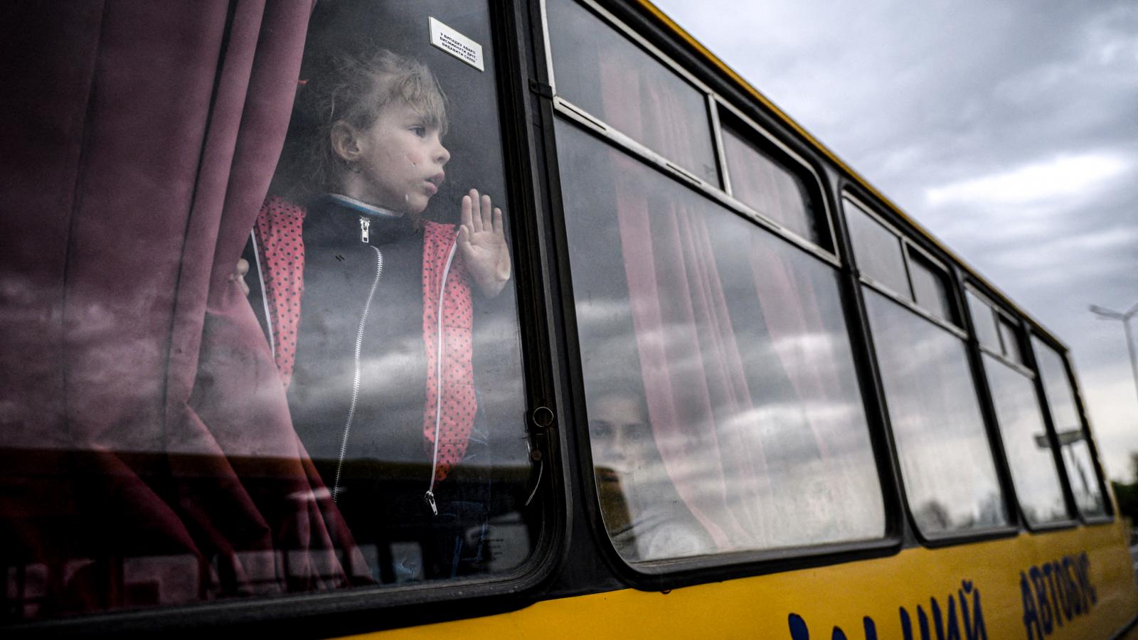 Egy lány néz ki egy buszból, miközben az orosz megszállás alatt álló zaporizzsjai területről származó családok érkeznek egy humanitárius konvojjal a belső menekültek regisztrációs és feldolgozó központjába Zaporizzsjában 2022. április 29-én, az Ukrajna el