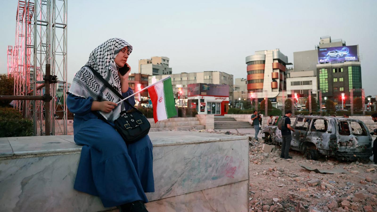Egy iráni nő egy felrobbantott jármű közelében ül a Hafteh-tir téren, Teheránban, 2025. június 23-án